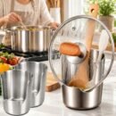 Compact stainless steel utensil holder on a kitchen counter holding wooden spoons and a spatula. A woman is chopping vegetables in the background. Product measures 4.92 inches high by 3.94 inches in diameter. Space-saving design for extra prep room.